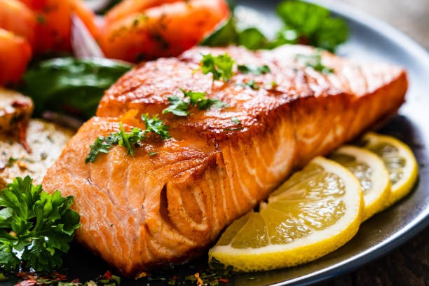 Cooked salmon on a plate with lemons and vegetable garnish