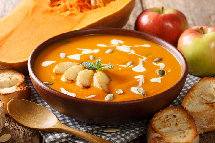 Butternut squash soup on table with ingredients around bowl