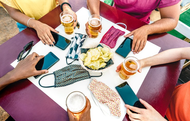 People at table with beers in one hand and phone in the other